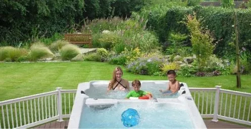 Drei Personen entspannen im Whirlpool mit Blick auf einen schönen Garten