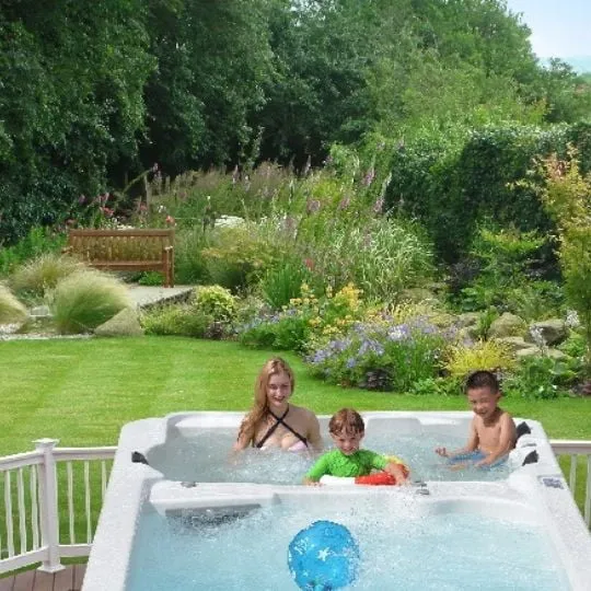 Drei Personen entspannen im Whirlpool mit bunten Bällen in einem üppigen Garten