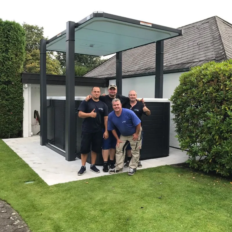 Vier Männer posieren vor einem modernen Gartenhaus mit Glasdach