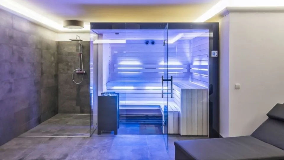 Moderne Sauna mit blauer Beleuchtung neben einer Glasdusche