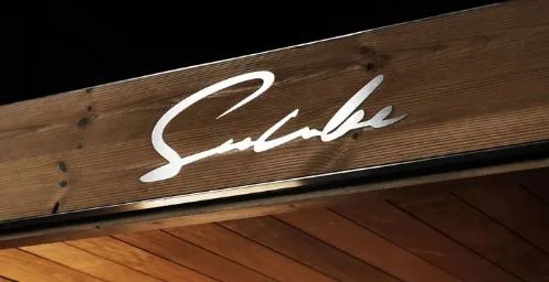 Weißes, geschwungenes Schriftzug-Logo auf rustikaler Holzoberfläche