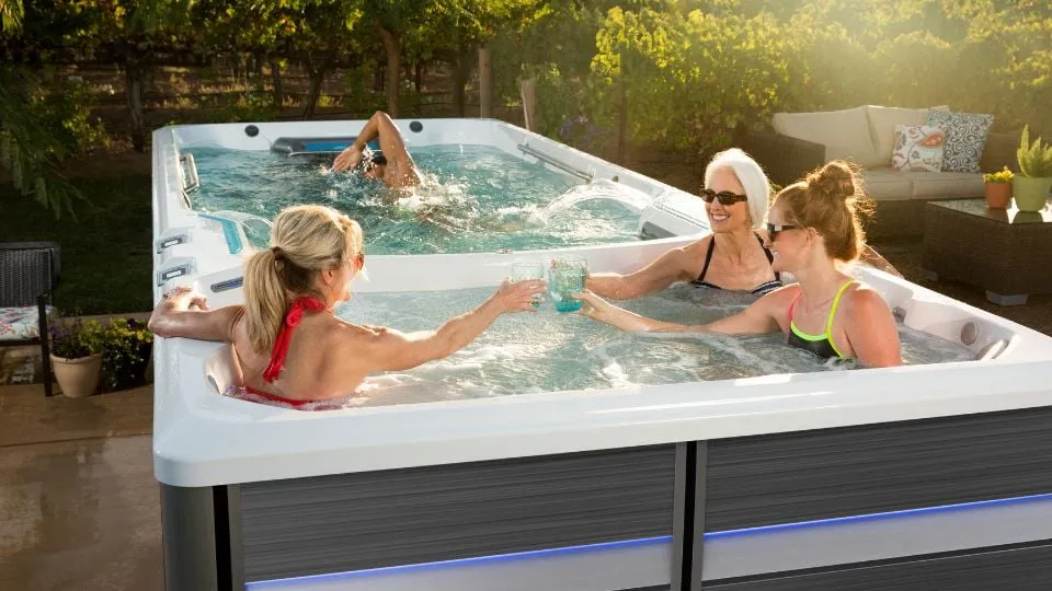 Drei Personen entspannen und schwimmen in einem Außen-Whirlpool im Garten