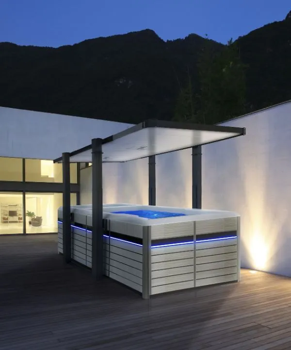 Moderner Whirlpool auf Holzterrasse bei Nacht mit Berglandschaft
