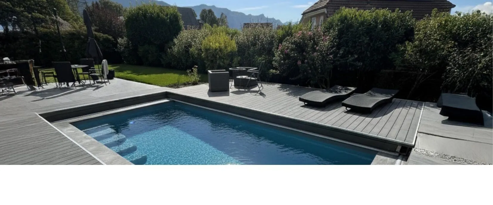 Eingelassener Pool mit grauer WaluDeck-Sicherheitsterrasse und Gartenmöbeln vor Bergkulisse