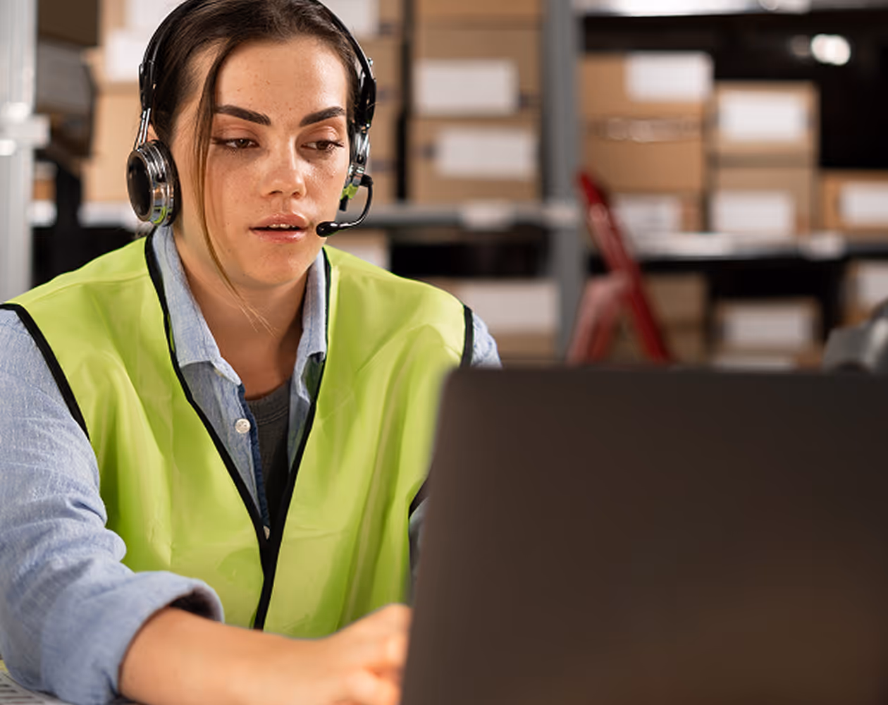 Une femme portant un gilet jaune et un casque travaille sur un ordinateur portable.