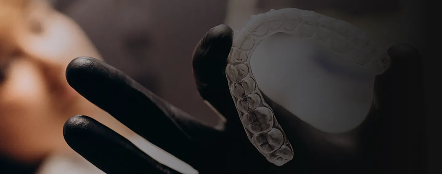 Zahnarzt mit schwarzen Handschuhen hält eine transparente Aligner-Zahnschiene vor einem Patienten