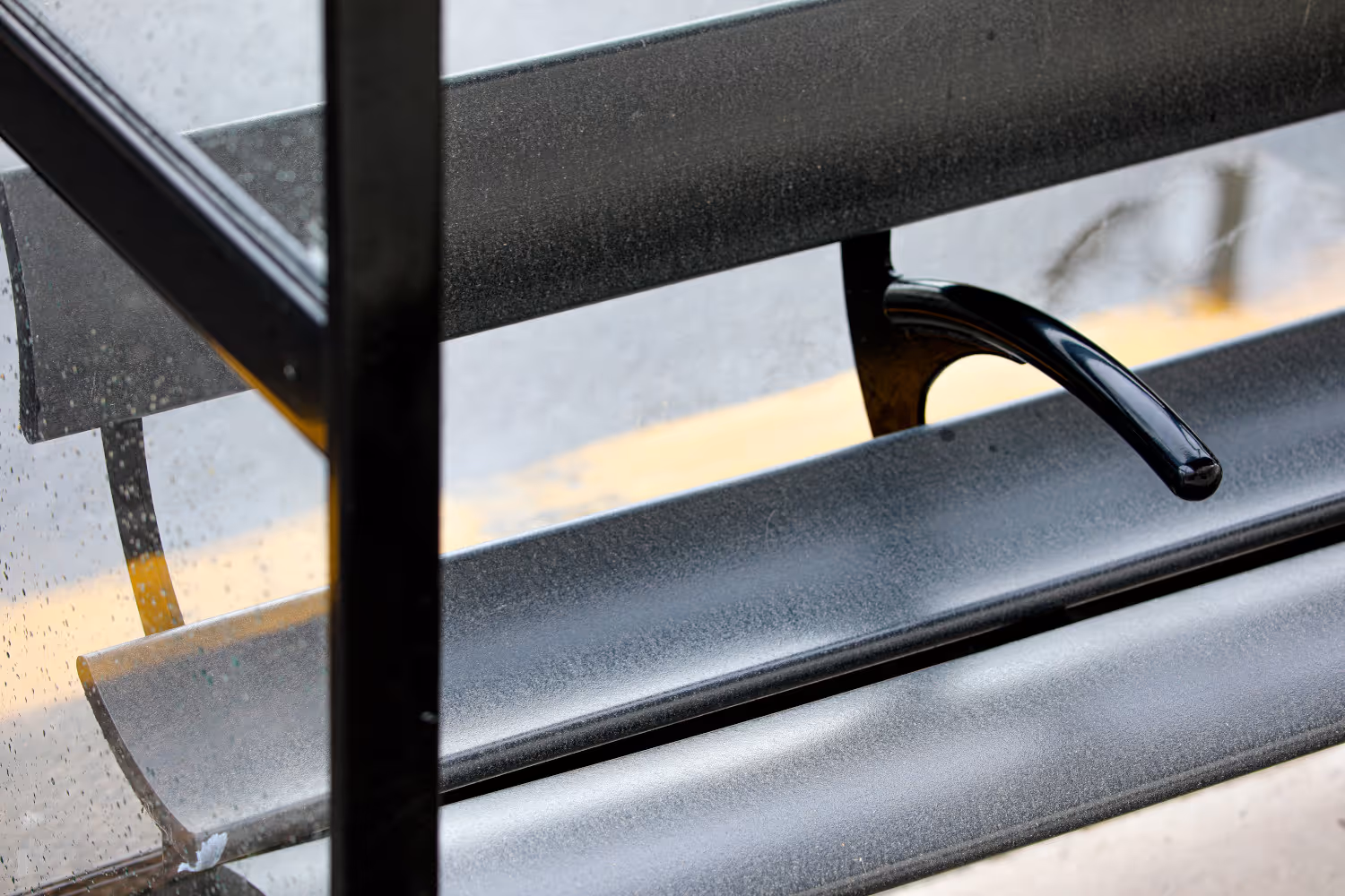 A zoomed image of a black bus shelter seat with an arm rest