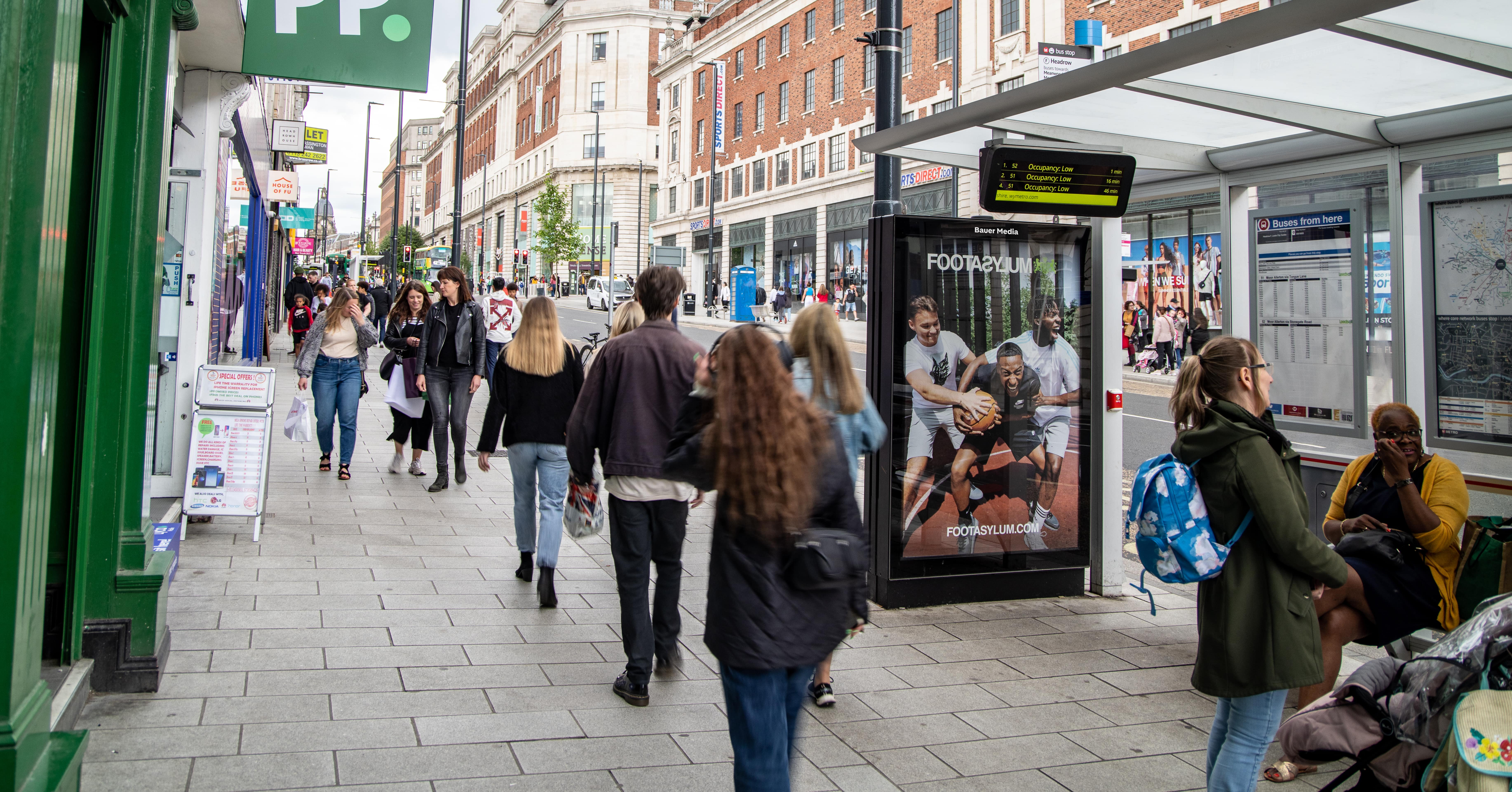 Footasylum ad at a bus shelter with people walking past
