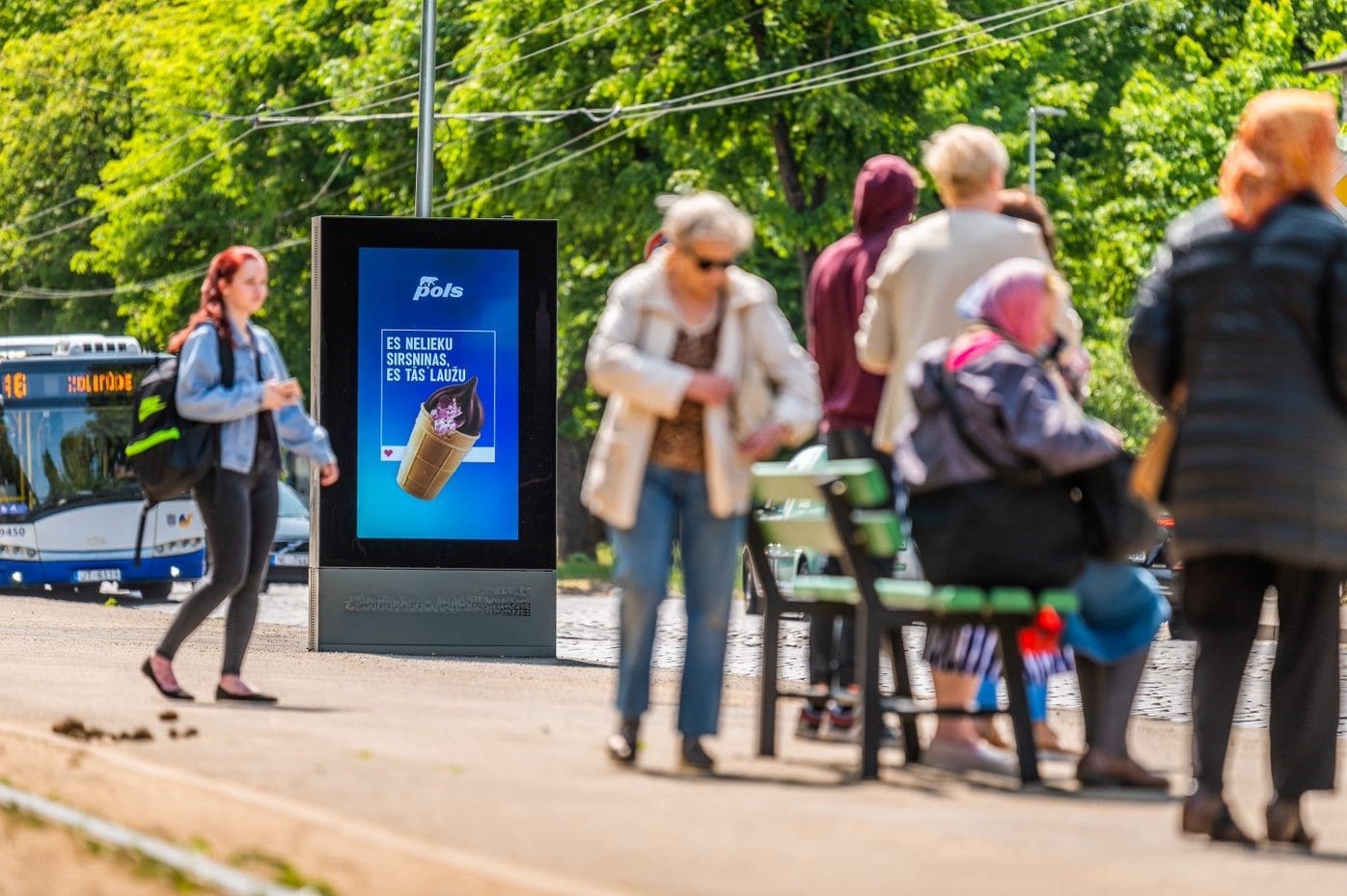A digital advertisement on a busy London road with people and traffic passing by