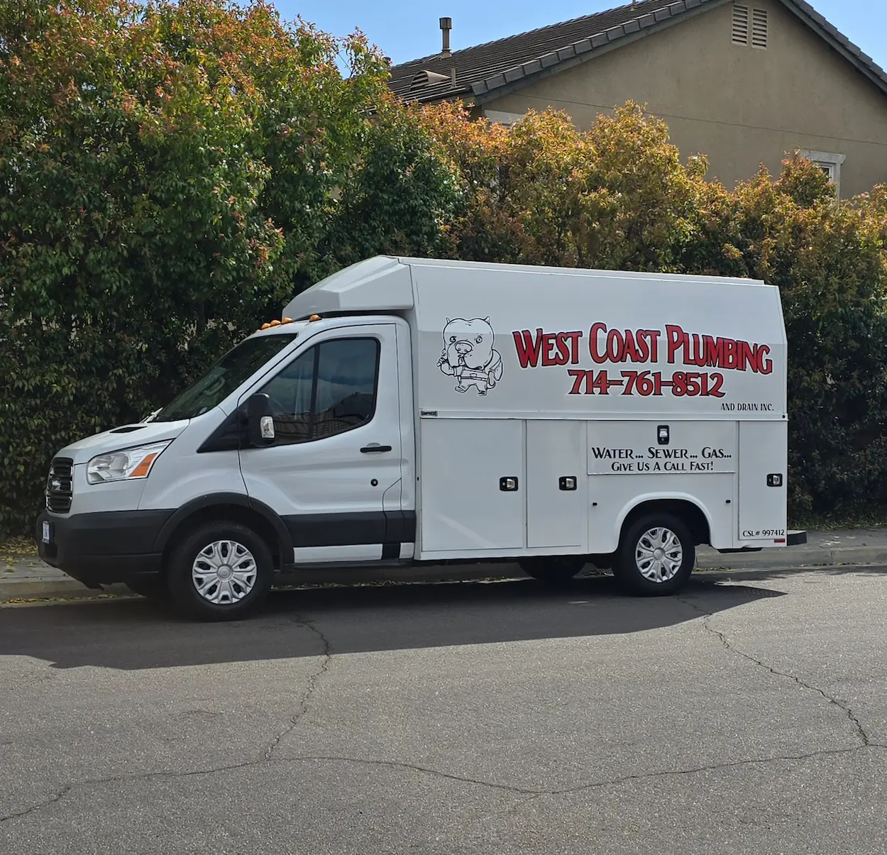 White West Coast Plumbing service van parked on a street with contact number 714-761-8512 and a cartoon bear logo.
