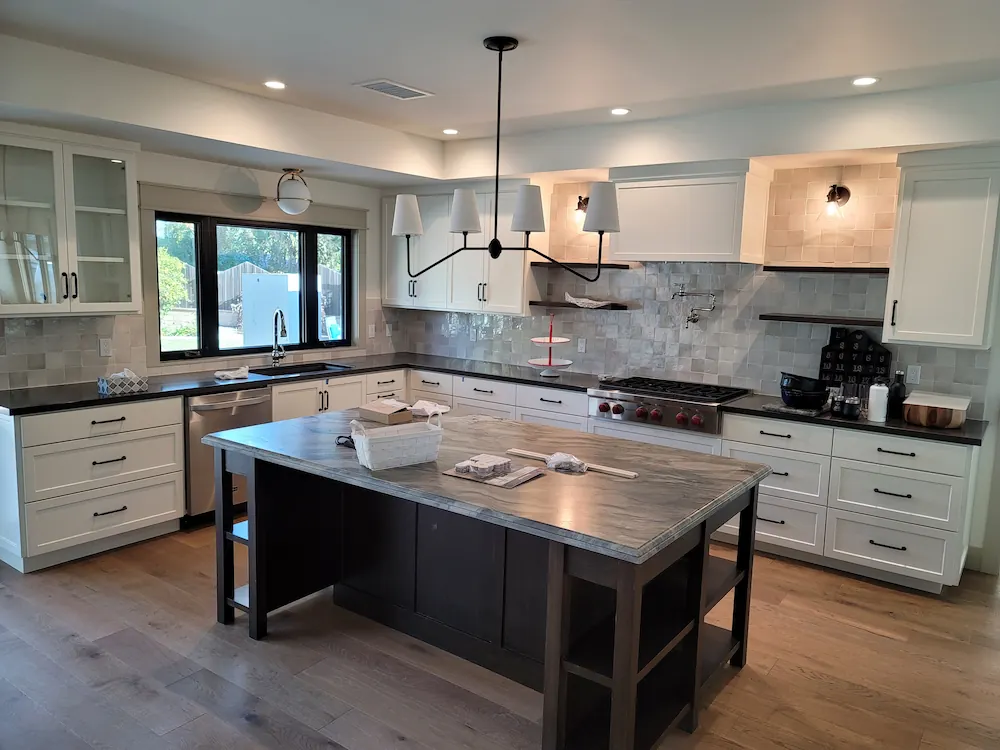 Modern kitchen with white cabinetry, black countertops, a large central island with a marble top, and a black chandelier with five shades.