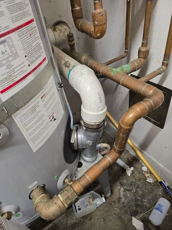 Close-up view of copper and PVC pipes connected to a water heater in a utility room.
