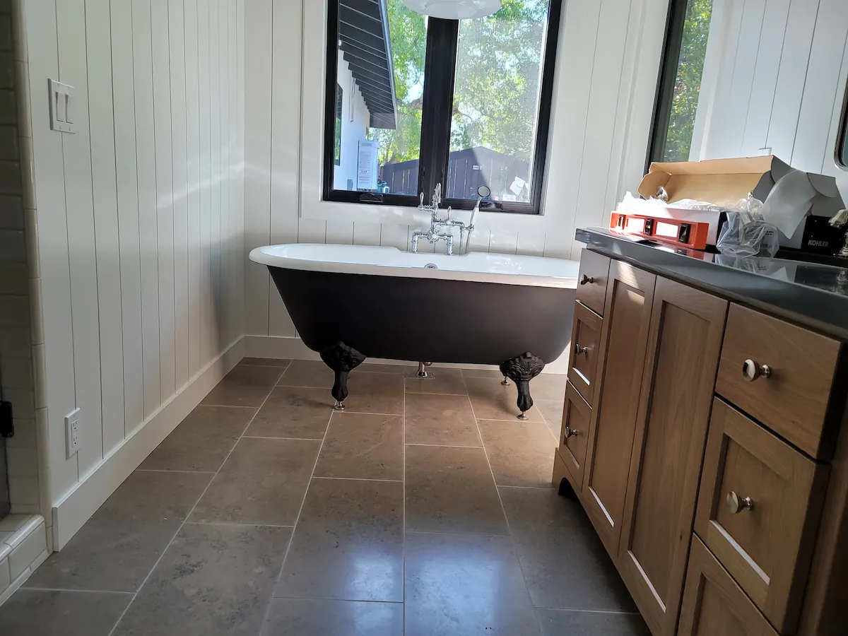 Bathroom with a black clawfoot bathtub under a window and wooden cabinets with a black countertop on the right.