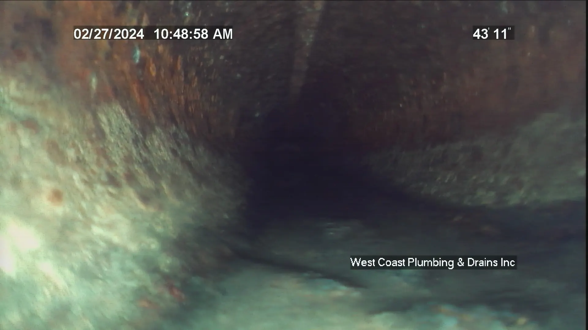 Inside view of a rusty and corroded sewer pipe with water at the bottom.