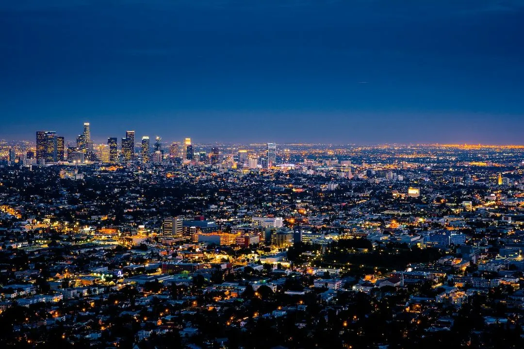 Nighttime cityscape of a large city with illuminated buildings and streets under a deep blue sky.