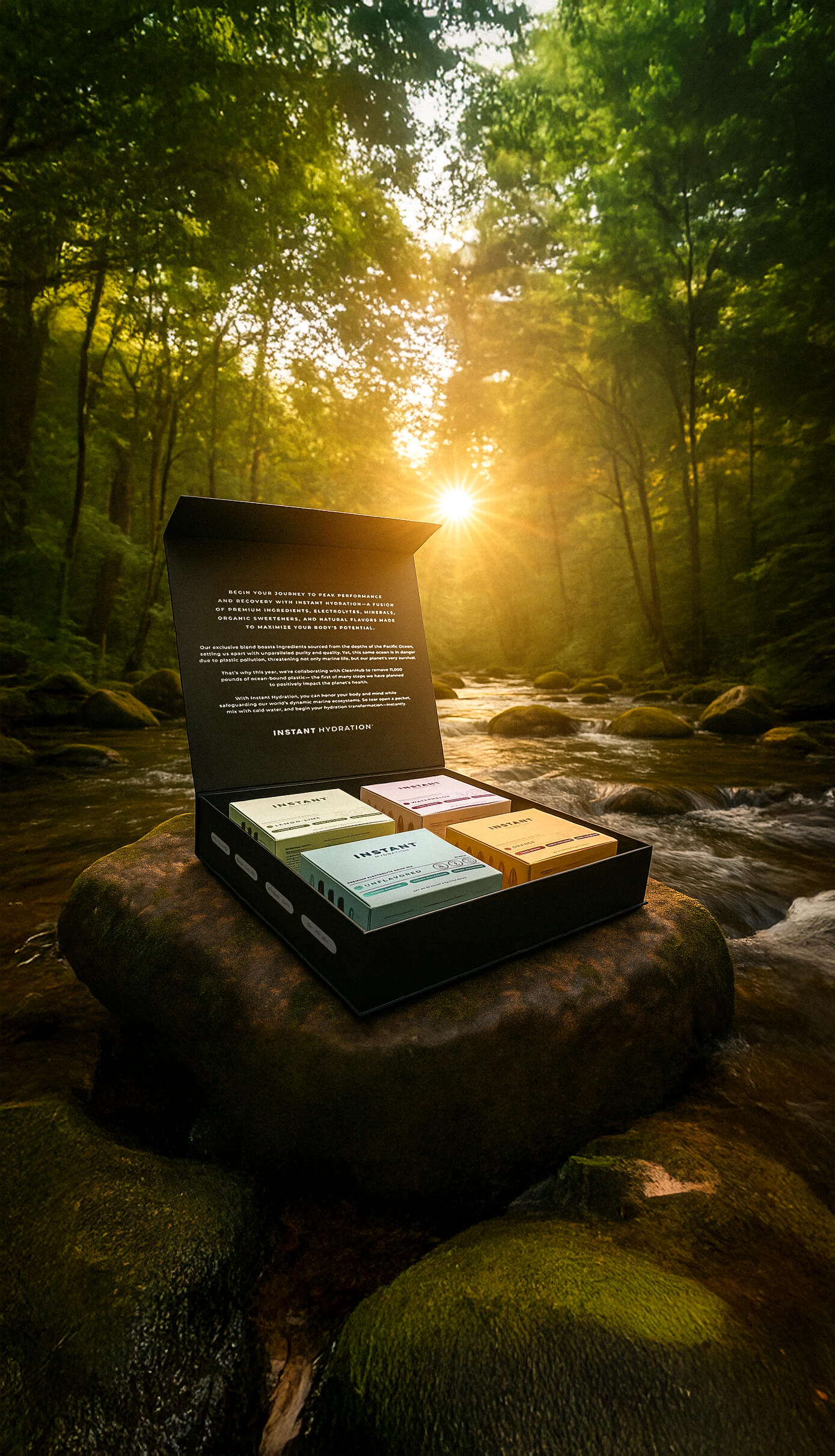 Open black gift box with four colorful hydration product packages placed on a mossy river rock with a sunlit forest and flowing stream in the background.