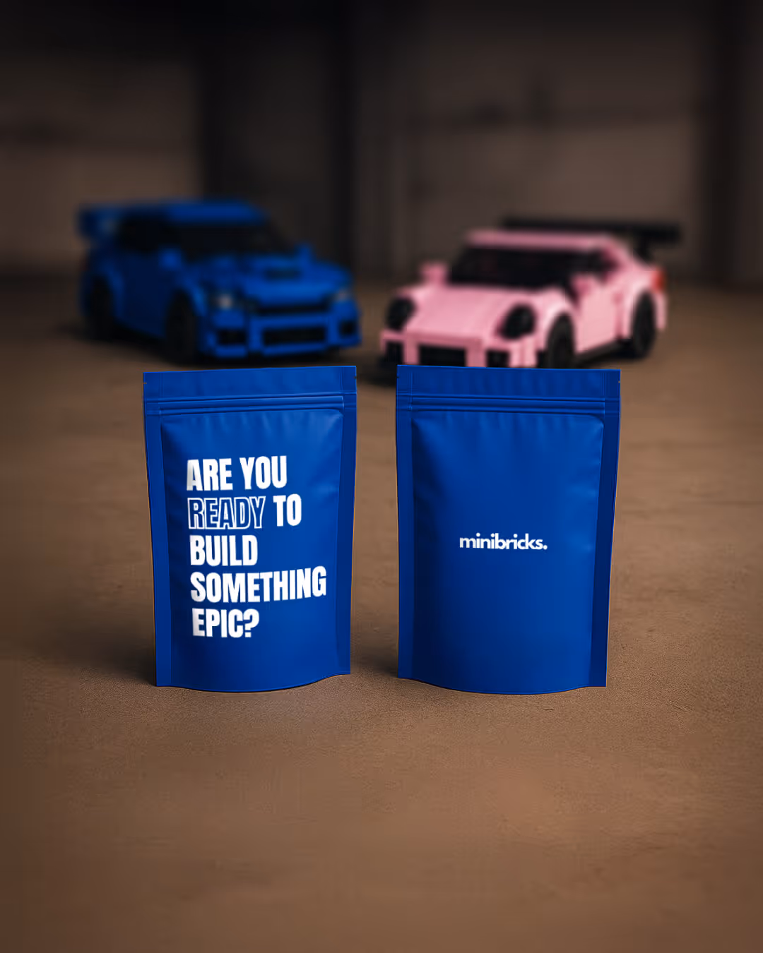 Two blue stand-up pouches with one pouch reading 'ARE YOU READY TO BUILD SOMETHING EPIC?' and the other labeled 'minibricks,' with two blurred toy cars in the background.