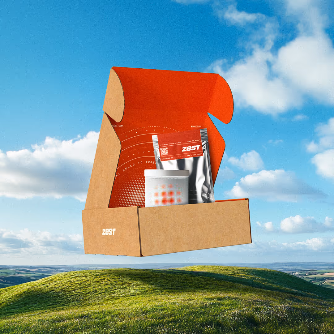 Open cardboard mailer box with red interior containing a white container and a silver pouch labeled Zest, floating over a green hill under a blue sky with clouds.