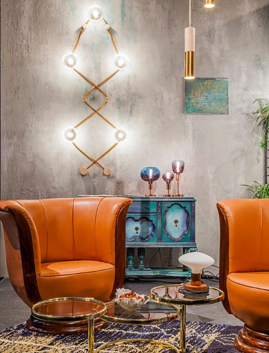 Modern living room with two orange leather armchairs, a round glass coffee table with gold legs, a blue vintage cabinet, and contemporary wall and pendant lights.