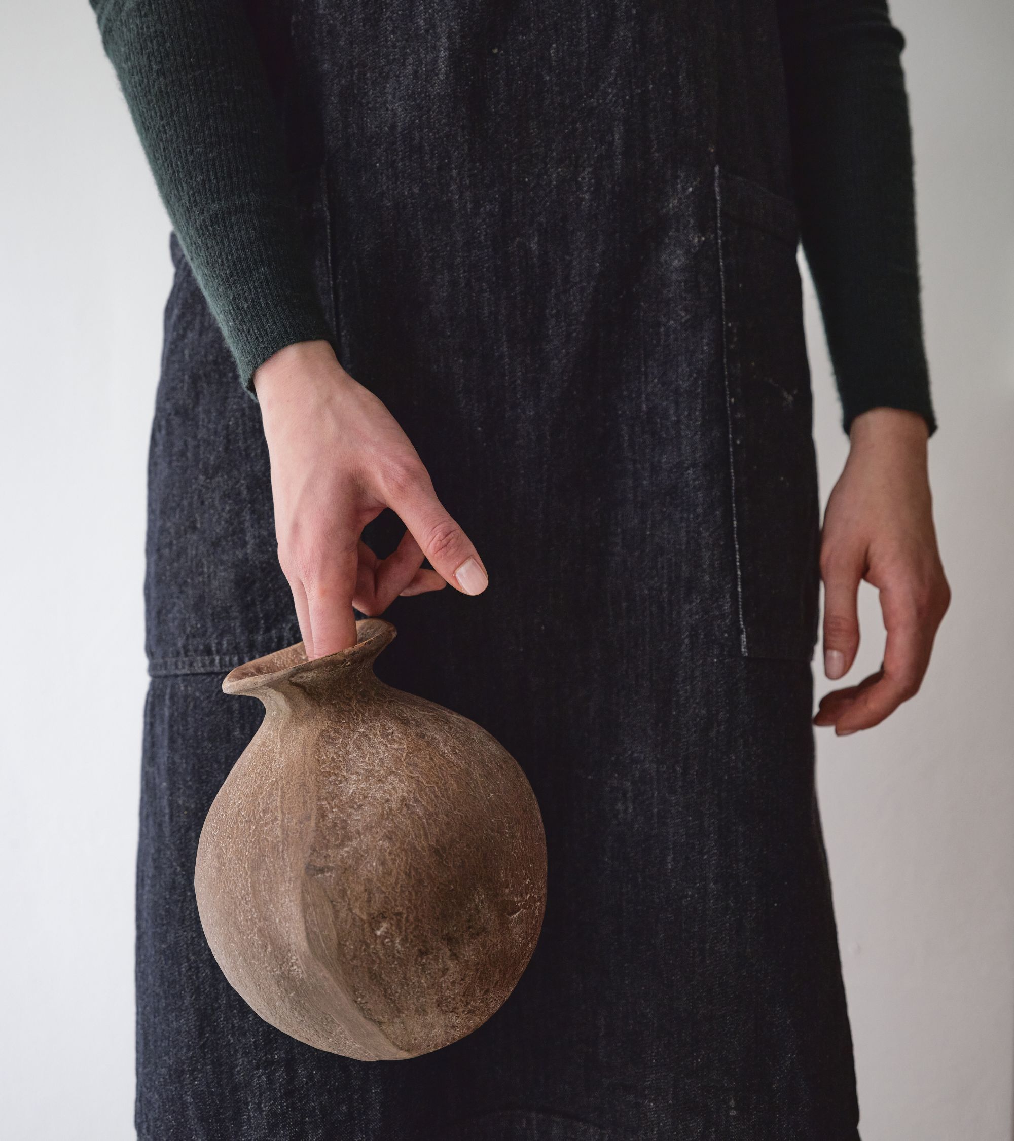 Person in dark clothing holding a rustic brown ceramic vase by its narrow neck.