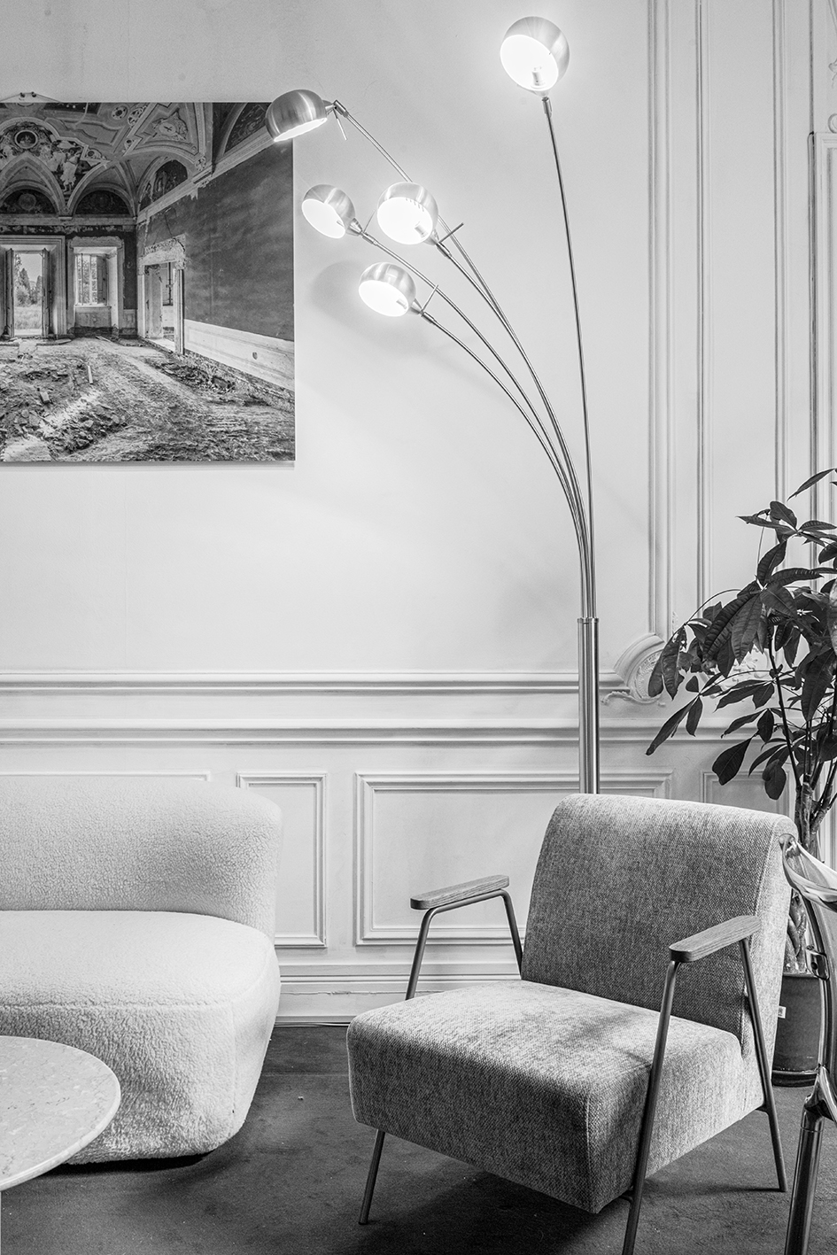 Photo d'un coin salon avec un fauteuil en tissu, un canapé moelleux, une lampe sur pied à plusieurs bras allumés, une plante verte et une peinture murale.