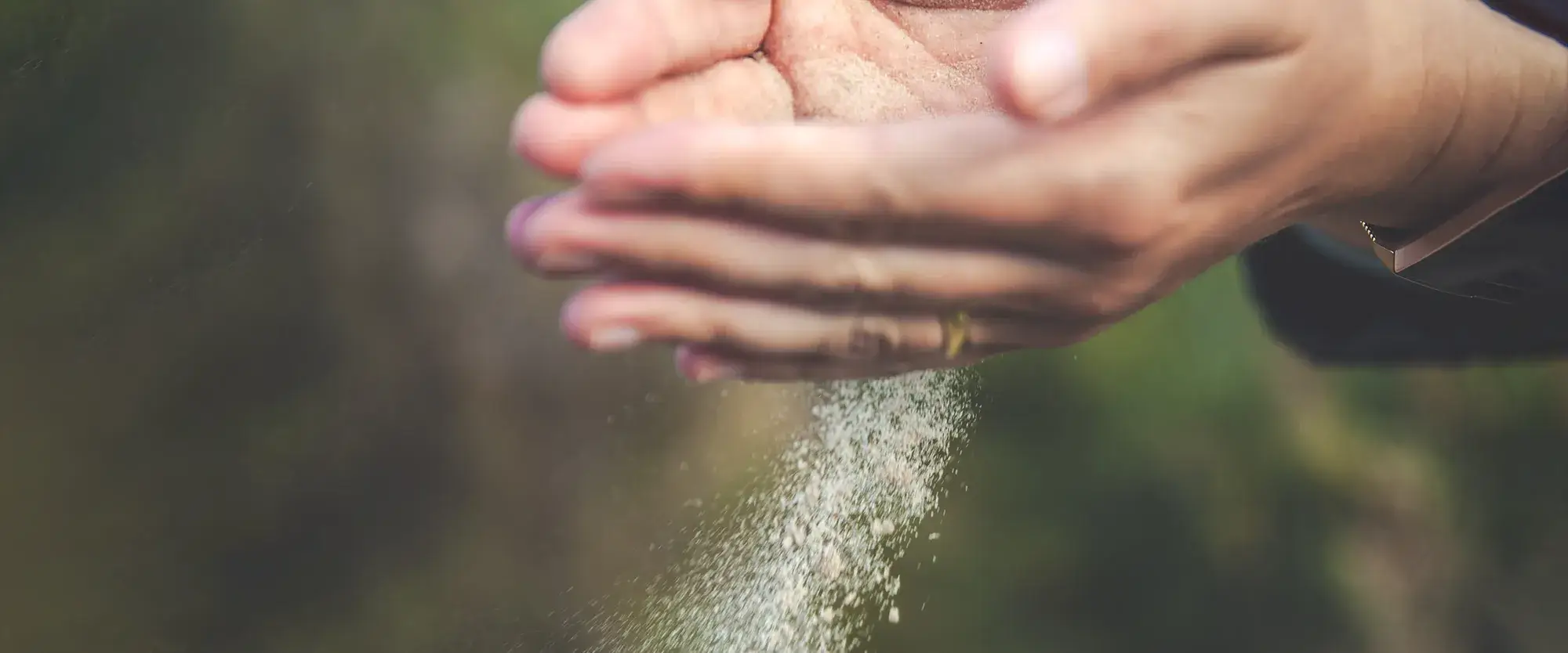 Hände mit rieselndem Sand vor grünem Hintergrund