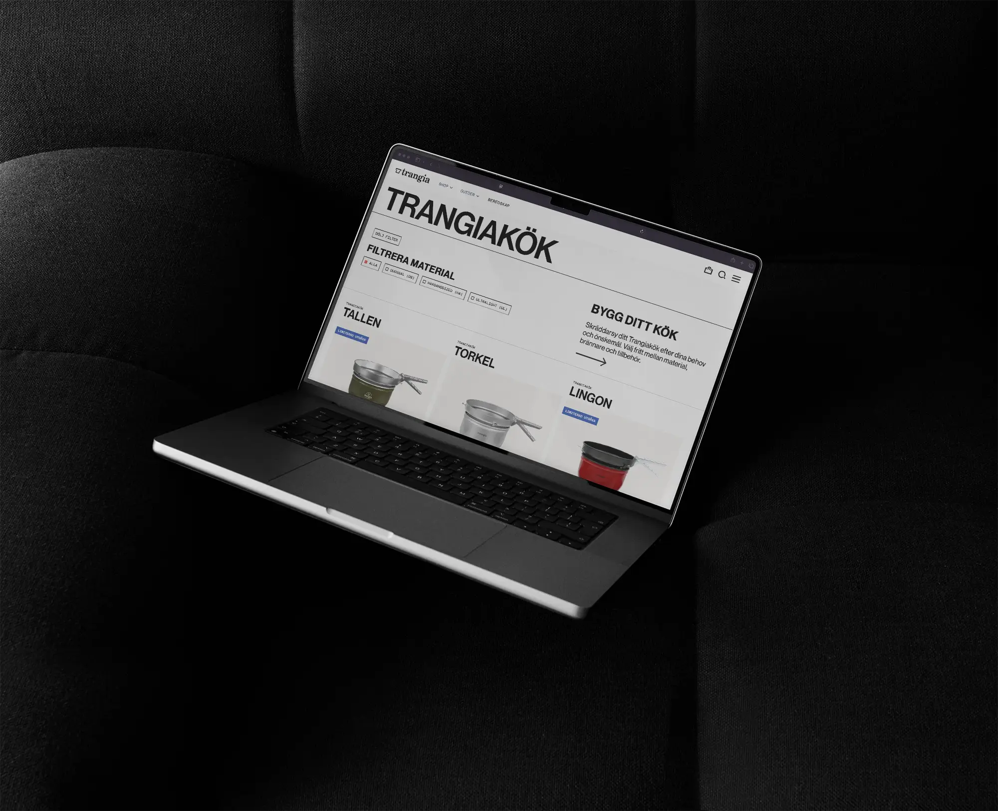A laptop displaying the Trangia kitchen website is placed on a black cushioned surface. The screen shows different cooking sets and related products with Swedish text.