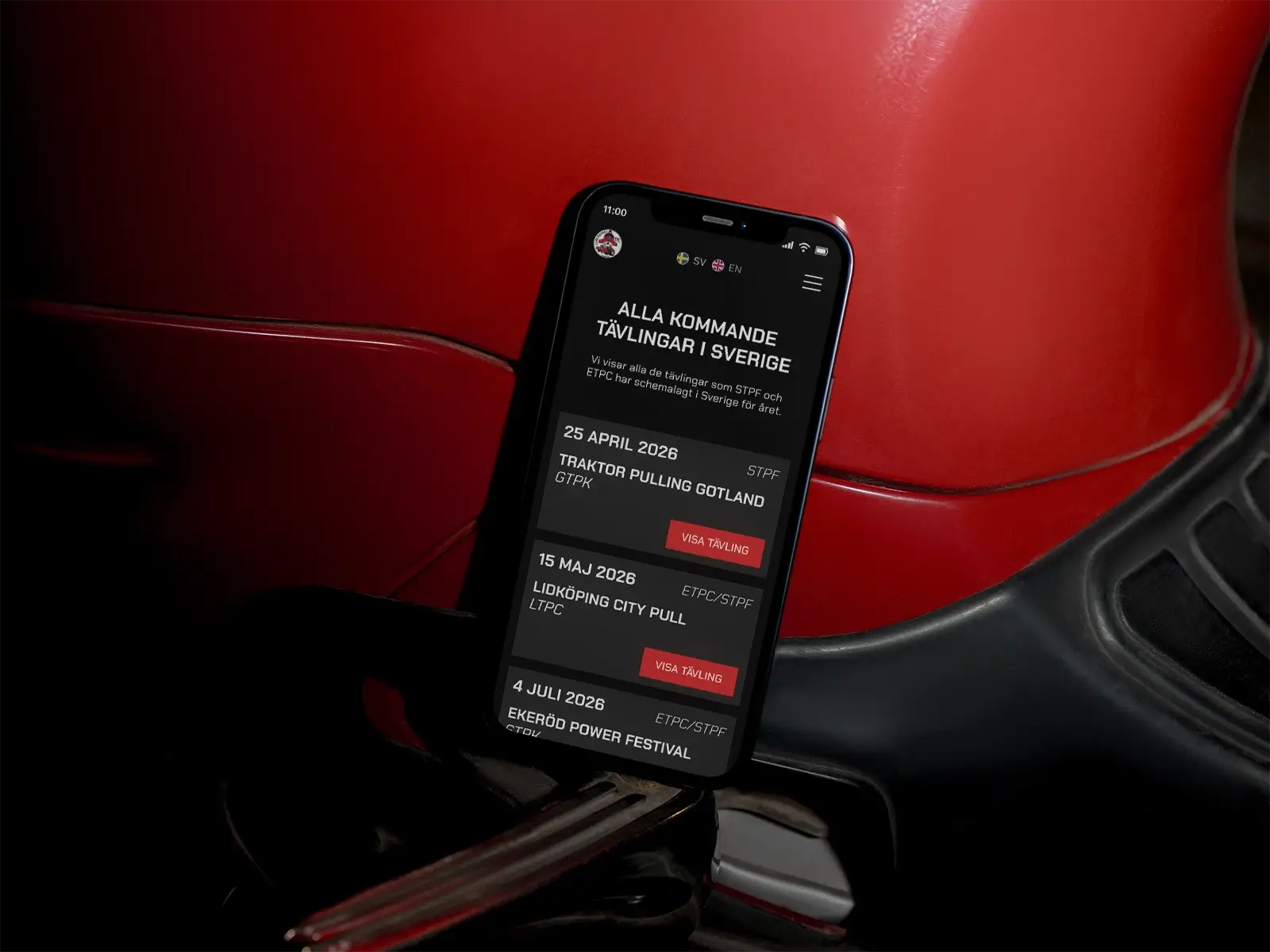 A smartphone displaying a list of upcoming competitions in Sweden rests against a red leather surface, a tractor seat, with event dates and locations visible on the screen.
