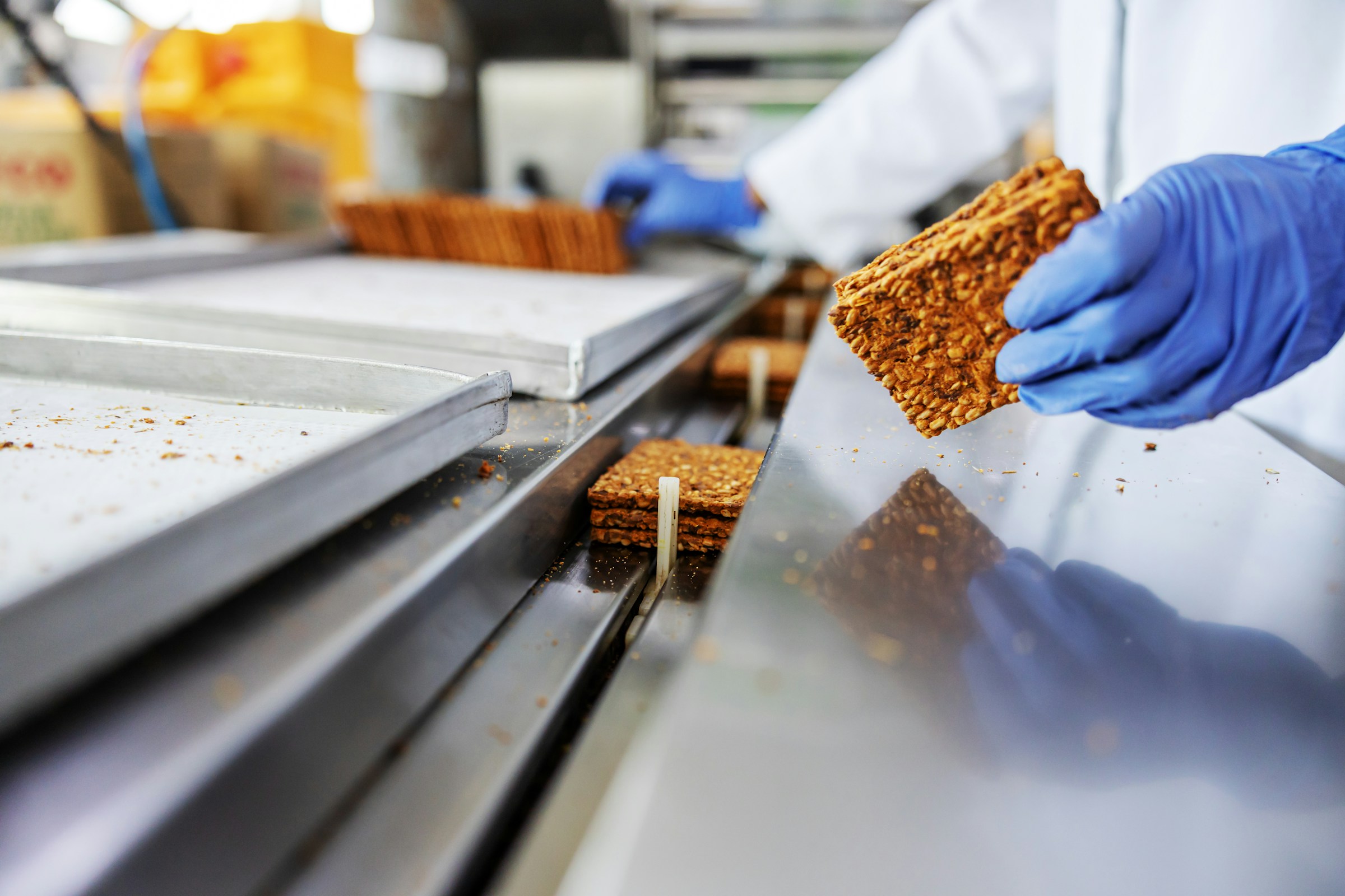 Person wearing blue gloves handling rectangular granola bars on a production line.