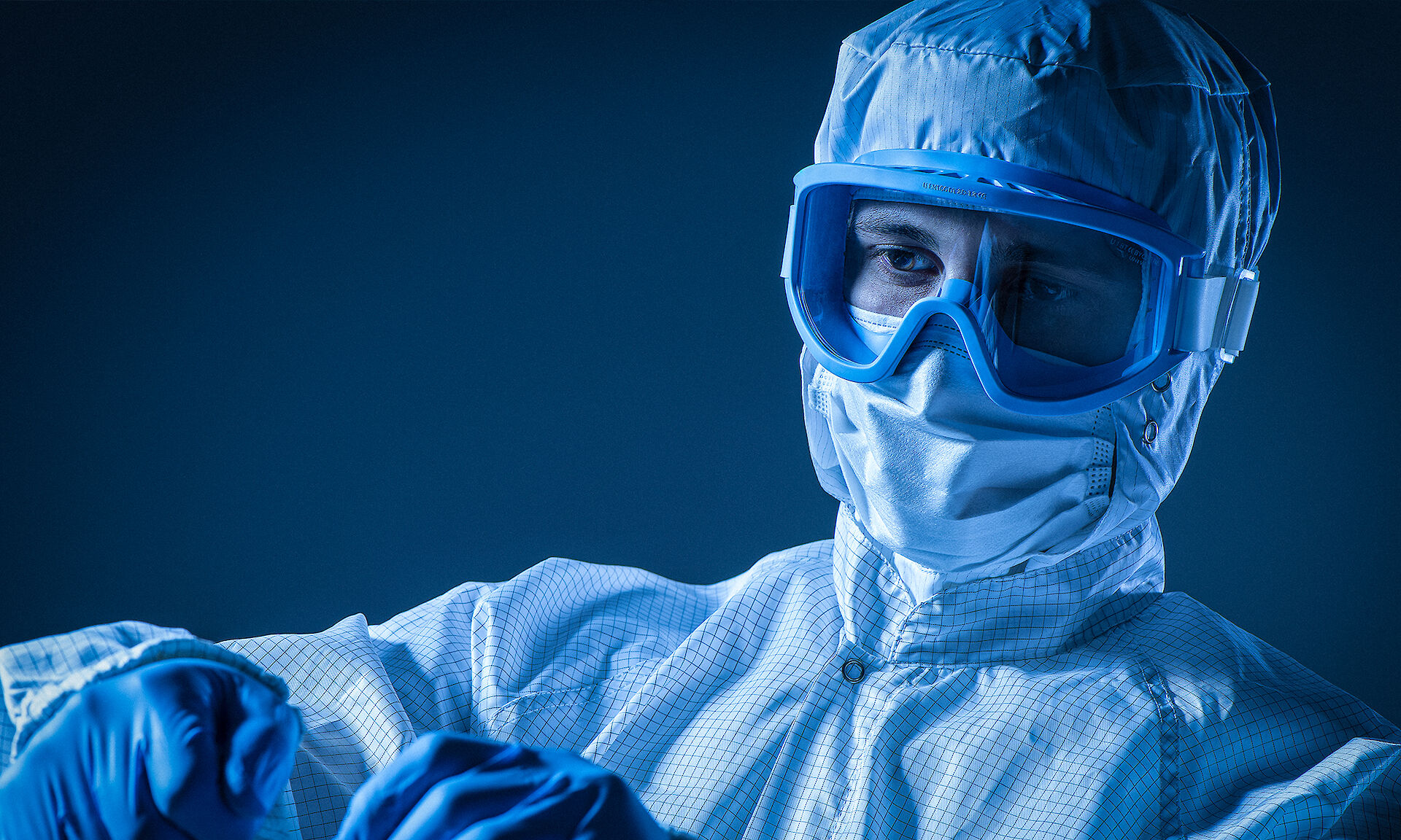 Scientist or technician wearing protective suit, mask, goggles, and gloves in a laboratory setting.