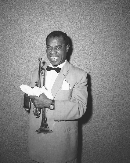 Black and white photo of a smiling man in a suit holding a trumpet and a cloth.