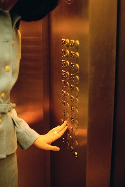 Person pressing buttons inside a copper-colored elevator with round, metallic floor buttons.