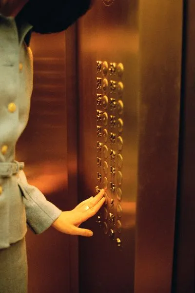 Person pressing buttons inside a copper-colored elevator with round, metallic floor buttons.