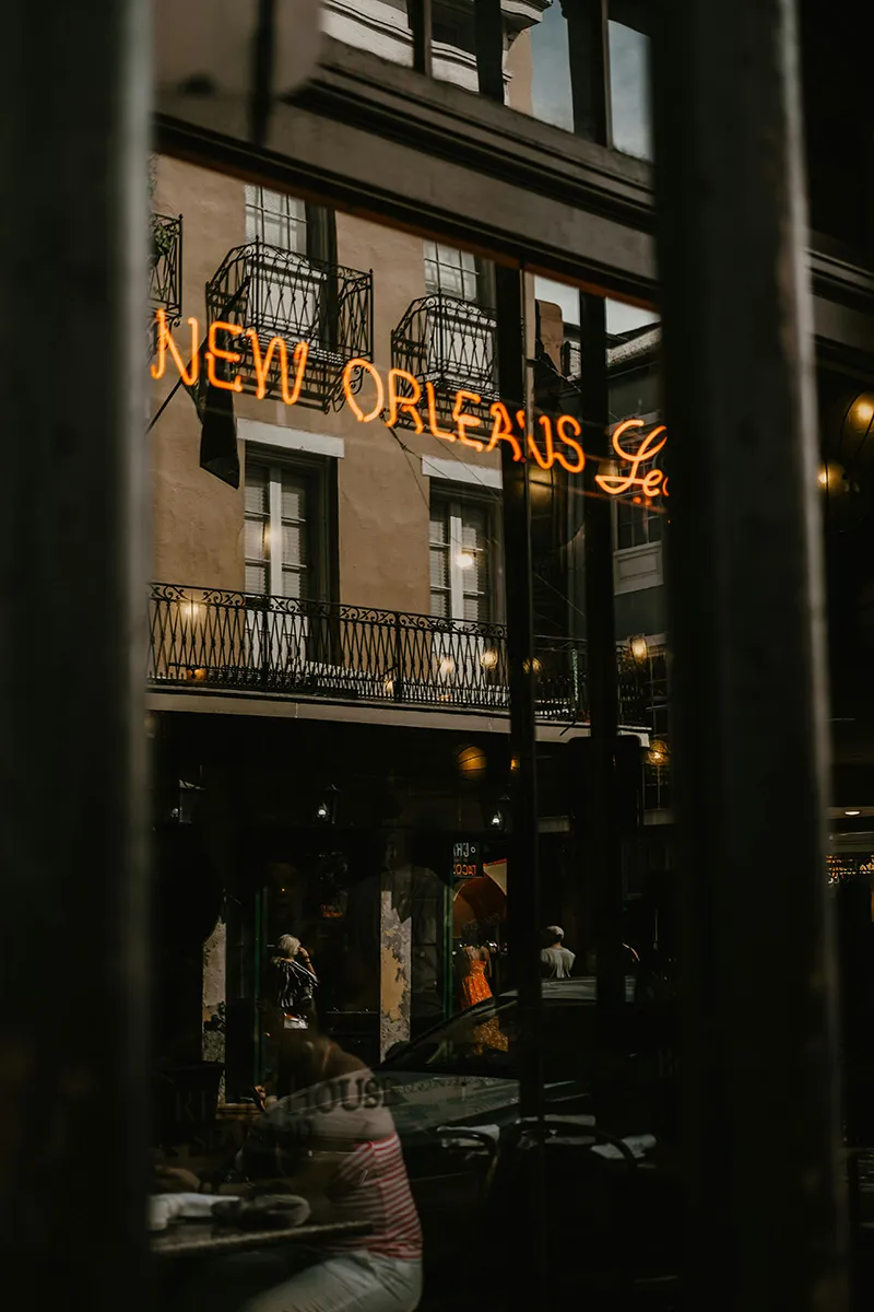 Reflection of a building facade with balconies and orange neon sign reading 'New Orleans' in glass.