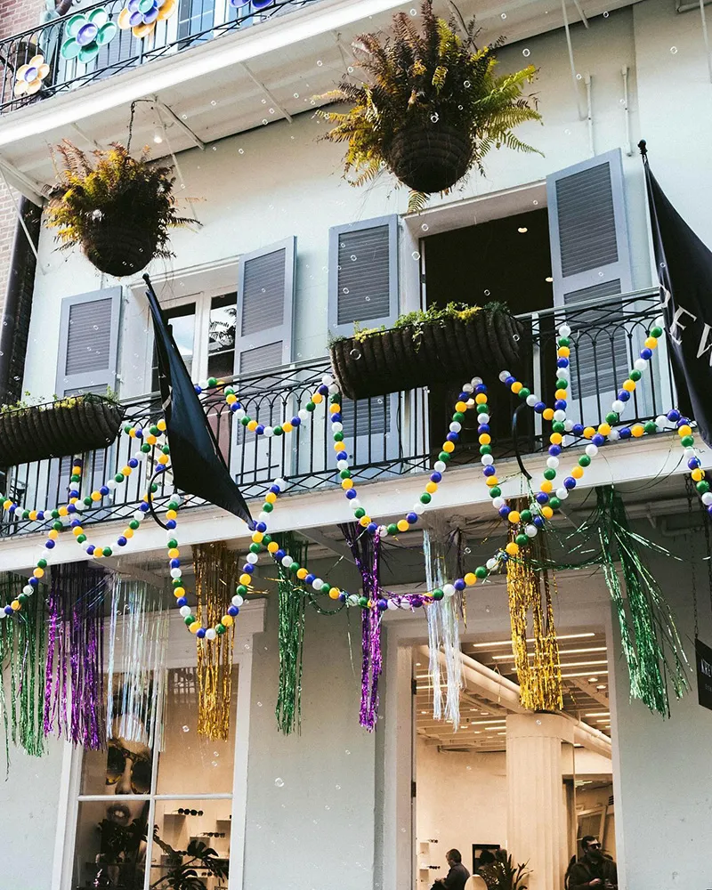 Balcony decorated with colorful Mardi Gras beads, hanging plants, and festive metallic streamers.