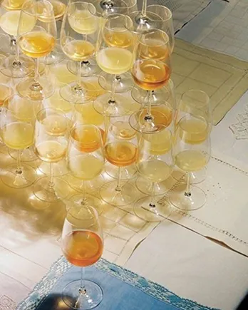Multiple wine glasses with varying shades of white and amber wine arranged on a tablecloth.