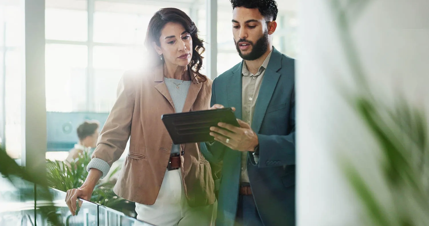 Two professionals stand indoors, looking at a digital tablet together.