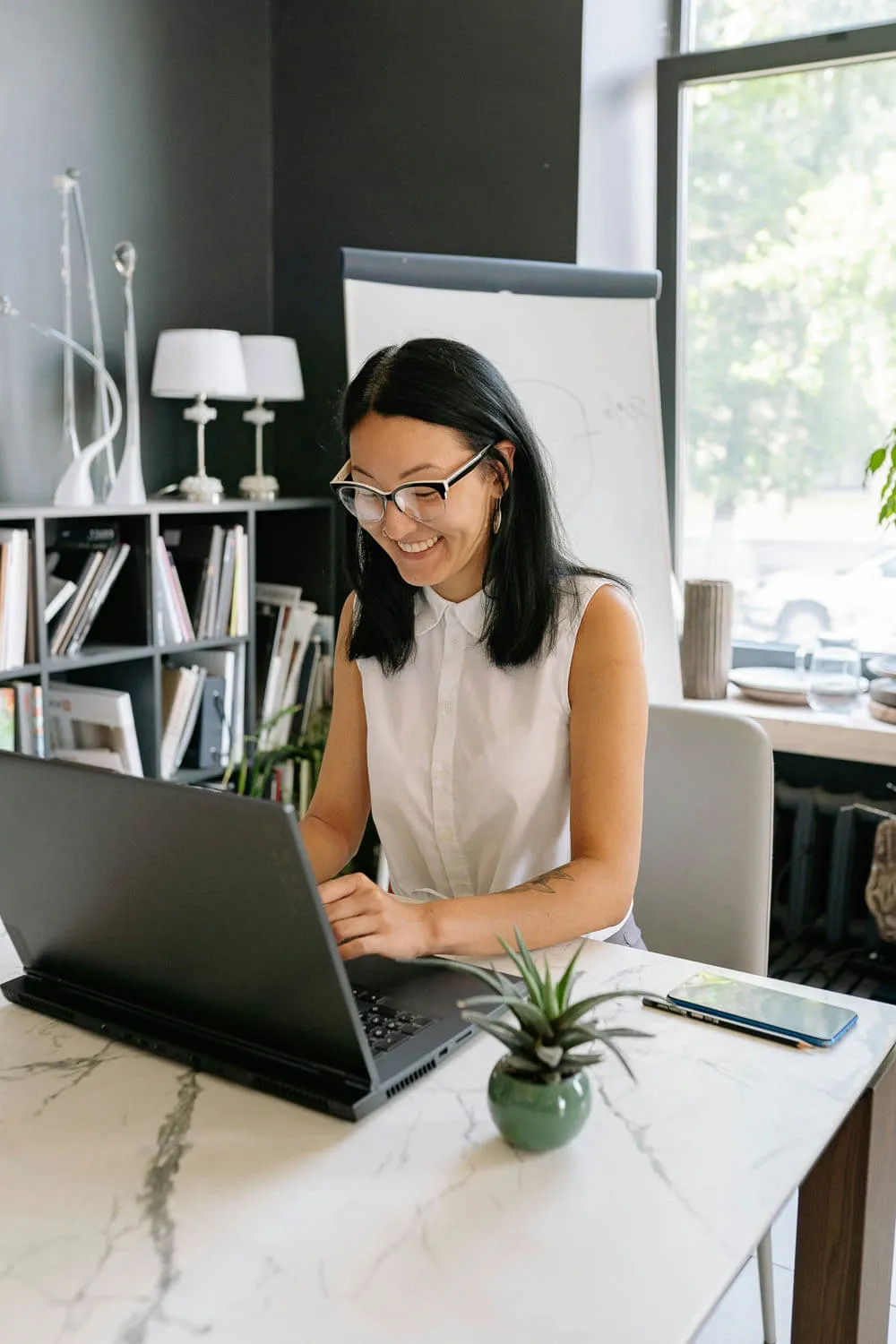 Woman wearing glasses and a sleeveless white blouse sits at a desk, reviewing her tax strategy.