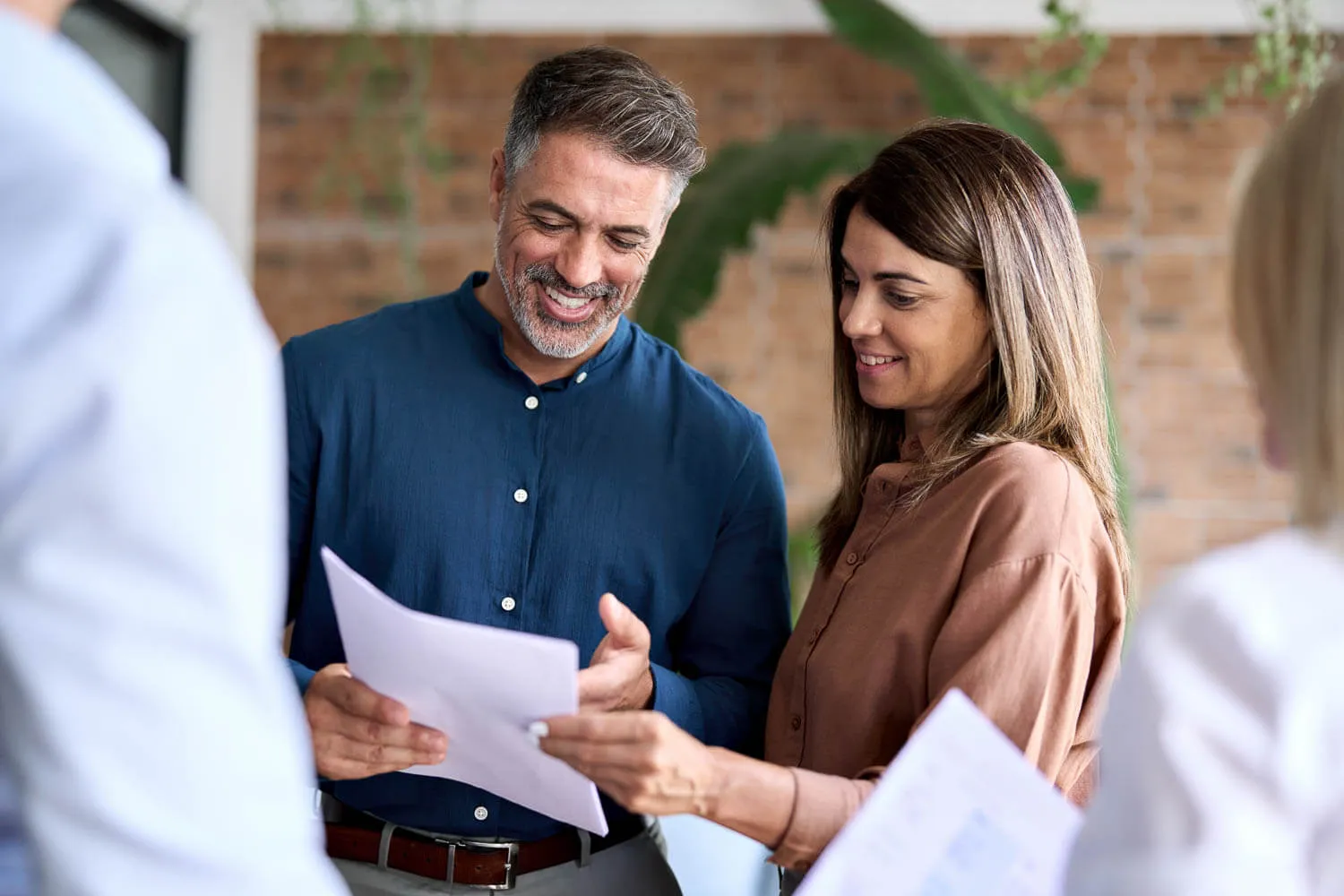 Two people standing, reviewing and discussing business report documents together while smiling.
