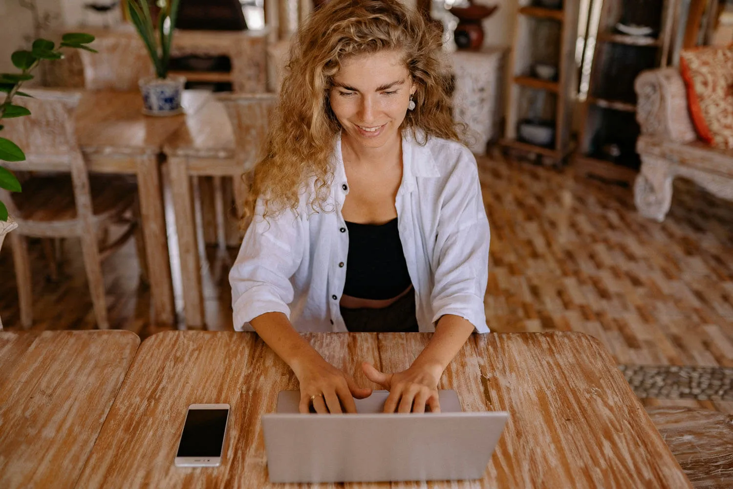 A woman with curly hair types on a laptop working on business bookkeeping.