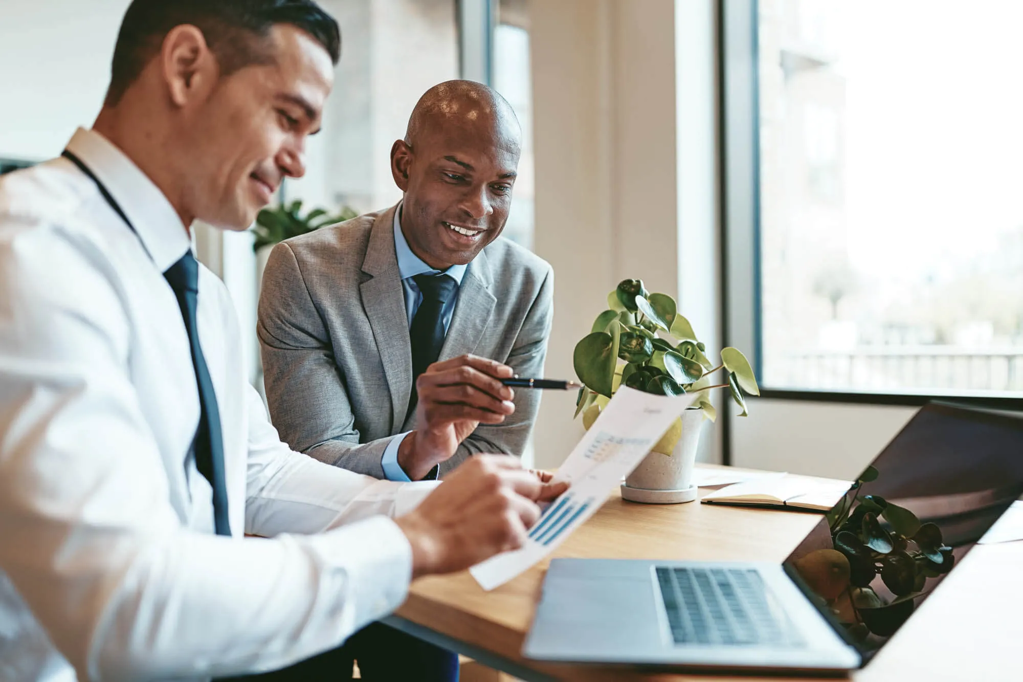Two men in business attire sit at a desk during a strategic financial business meeting.