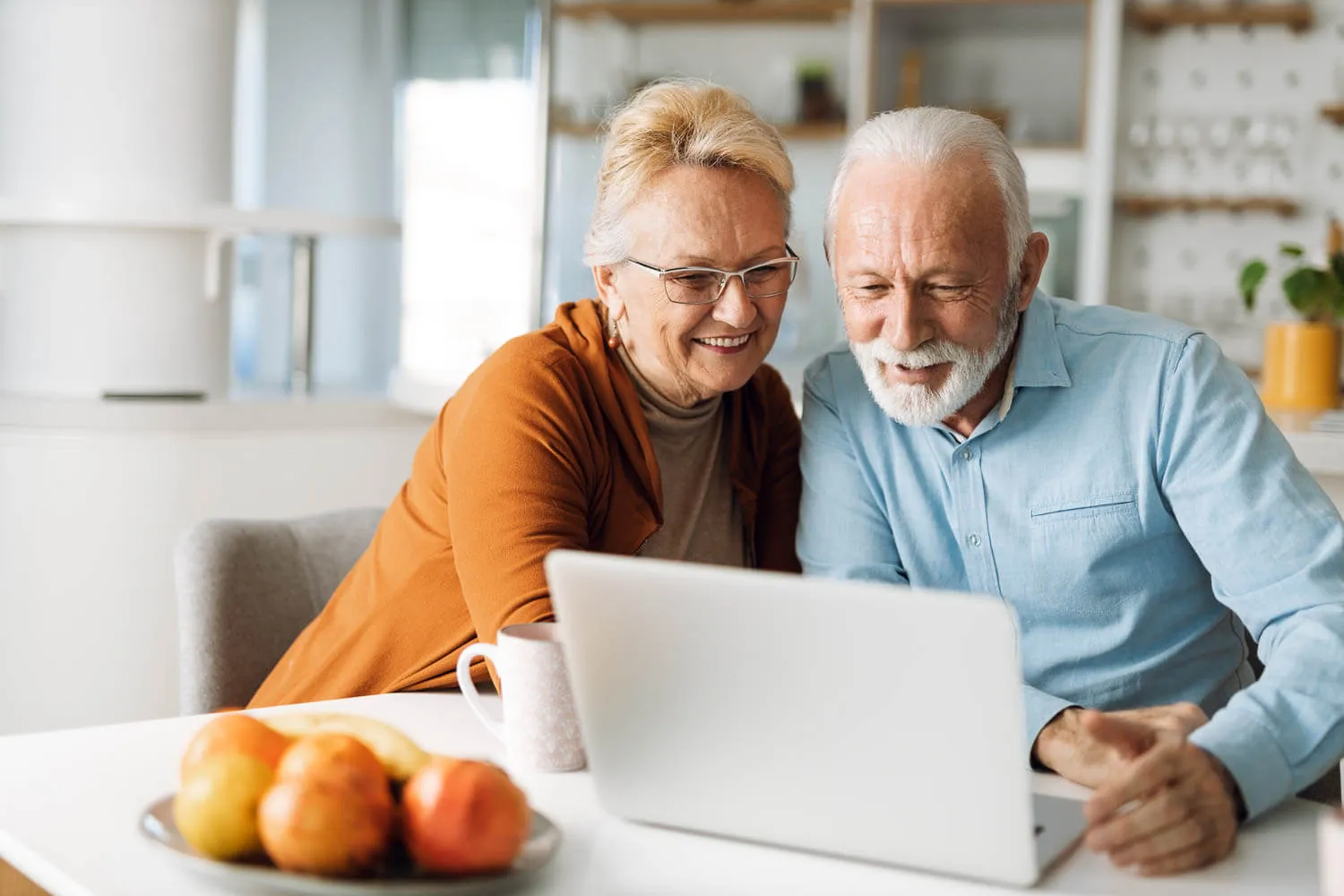 An retired man and woman sit at a table, smiling while facetiming their tax accountant.