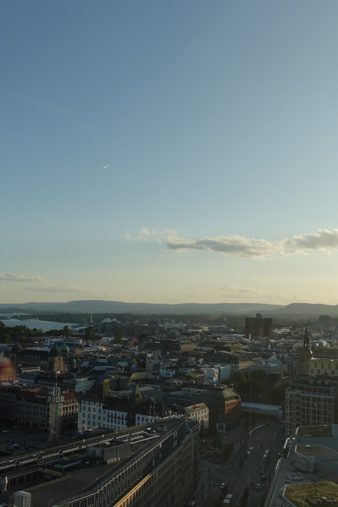 Cityscape view with buildings, roads, and distant mountains under a clear evening sky.