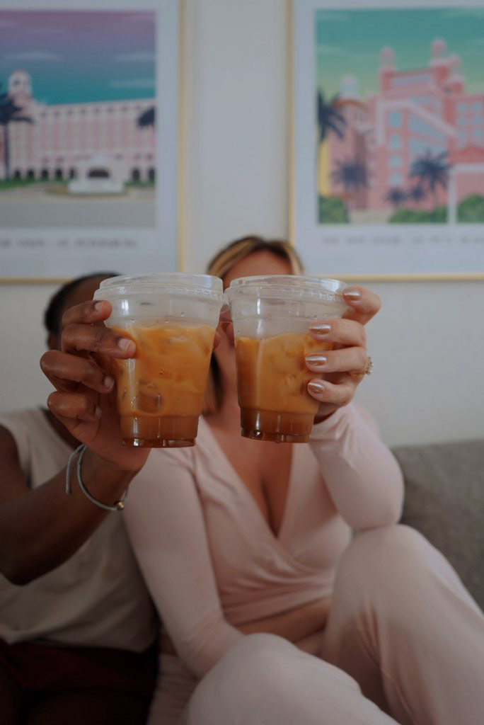 Friends toasting iced lattes from Sunkissed Brew while relaxing on a couch