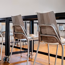 Two modern chairs with curved backs and metal legs placed near a black table on a wooden floor.