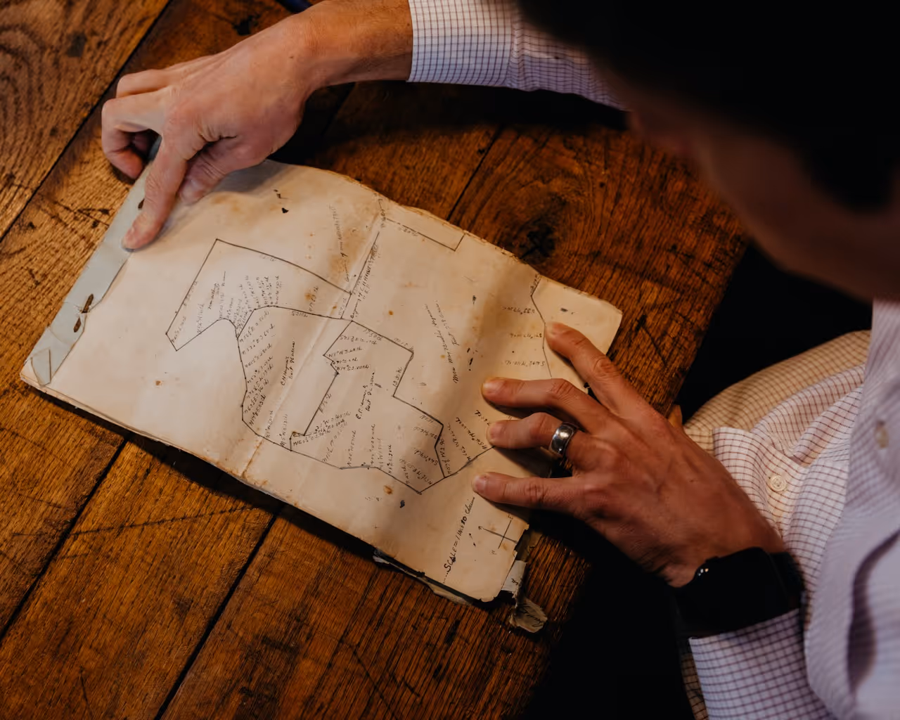 Hand flipping through architectural blueprints on a wooden table.