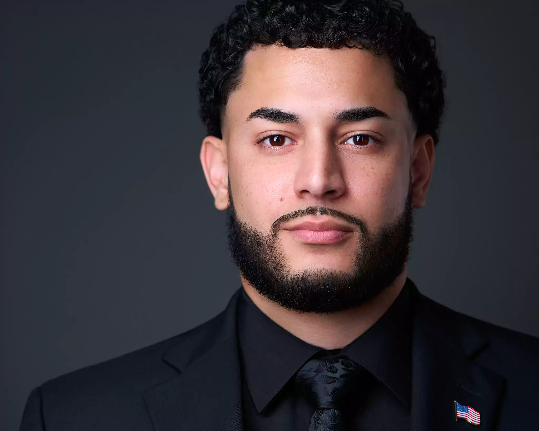 A man wearing a suit and tie with a flag pin on his lapel.