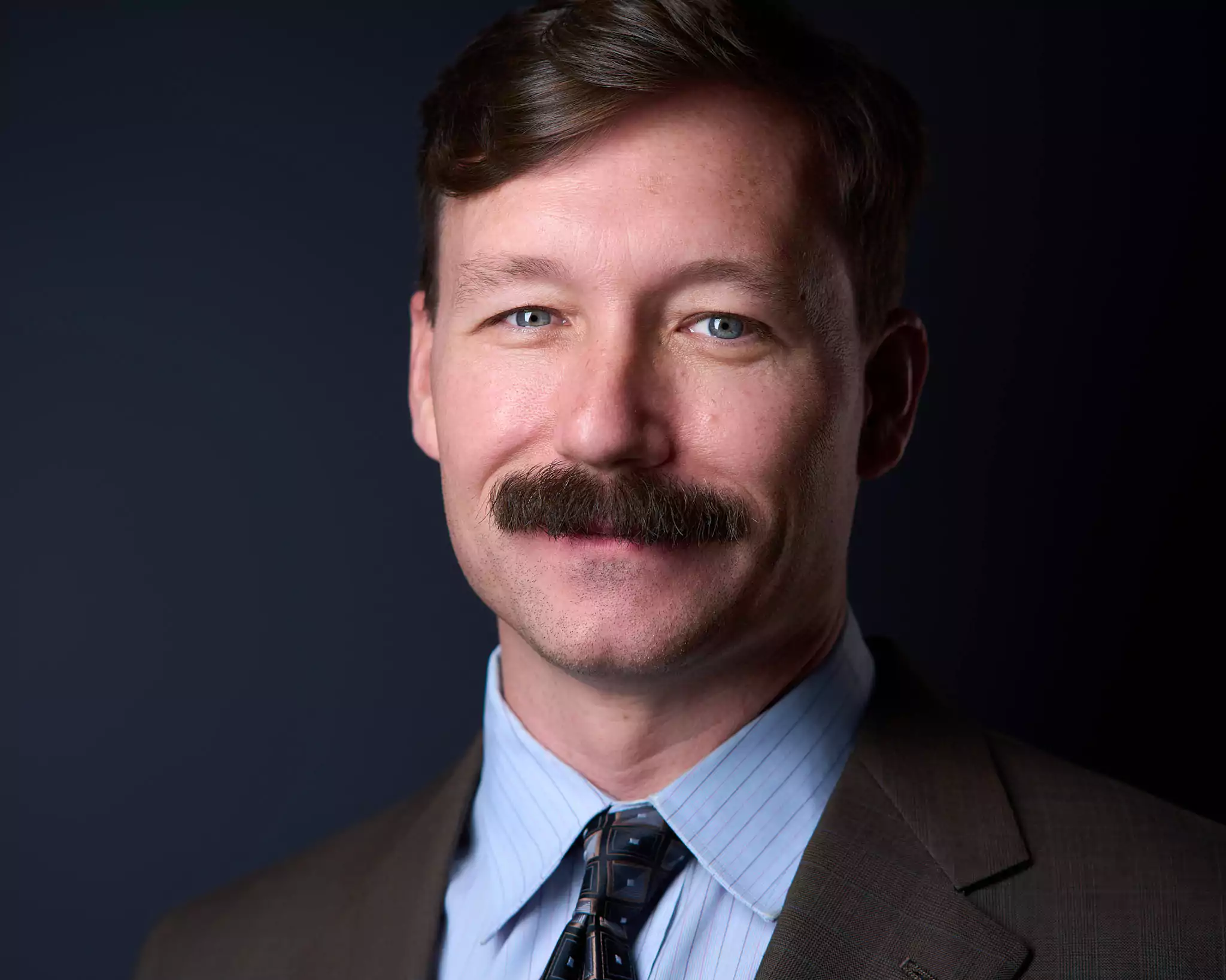 A man with a mustache and blue tie.