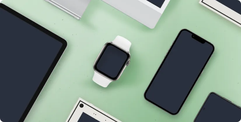 Various modern electronic devices including a smartwatch with a white band, a smartphone, a tablet, and other gadgets arranged on a light green surface.