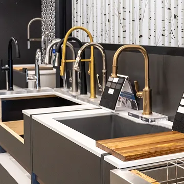 Modern kitchen sink display featuring brass and stainless steel faucets in The Water Closet showroom.